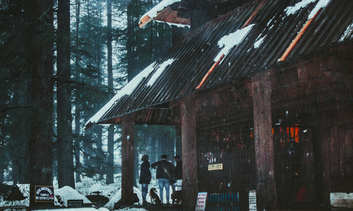 A couple standing outside a cozy snow-covered cabin, enjoying the winter scenery together.